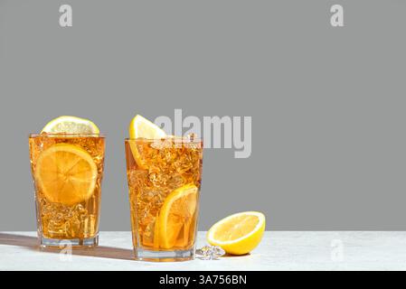 Thé glacé au citron. Verre de thé glacé sucré avec des tranches de citron et de la glace écrasée sur fond gris neutre à la mode. Boisson fraîche d'été maison. Banque D'Images