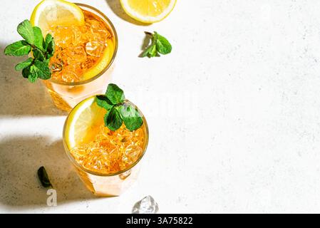 Thé glacé au citron. Verres de thé glacé avec des tranches de citron, de la menthe et des glaçons sur fond blanc, lumière dure à la mode avec des ombres, vue de dessus, copie spac Banque D'Images