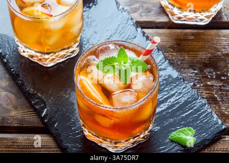 Thé glacé à la pêche. Verres de thé glacé sucré avec des tranches de pêche, de la menthe et de la glace écrasée sur fond d'ardoise, vue de dessus. Boisson fraîche d'été maison. Banque D'Images