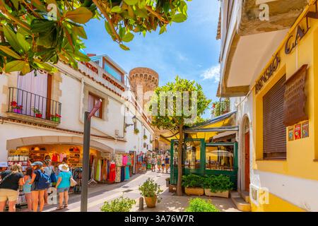 Rues étroites de boutiques et de cafés de trottoir dans la vieille ville blanchie à la chaux de Tossa de Mar Espagne, Costa Brava, avec la tour du château du 12ème siècle derrière. Banque D'Images