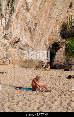 Les grimpeurs escaladent le mur de calcaire escarpé de la plage de Tonsai tandis qu'un ancien solarium se détend à proximité Banque D'Images