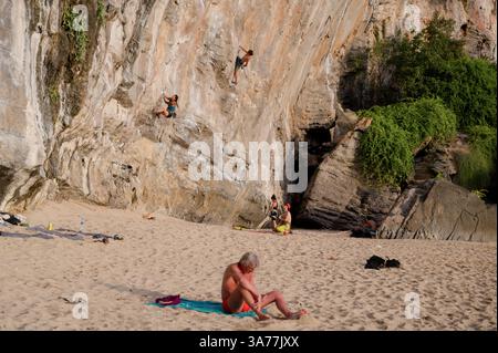 Les grimpeurs escaladent le mur de calcaire escarpé de Tonsai Beach tandis qu'un baigneur de soleil se détend à proximité Banque D'Images
