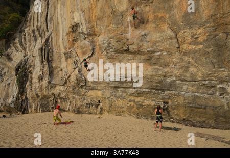 Les grimpeurs escaladent les superbes falaises calcaires de Tonsai, tandis que les gardiens veillent sur le sable Banque D'Images