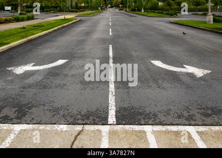 Deux flèches directionnelles s'écartant à gauche et à droite l'une de l'autre sur une surface de route. Banque D'Images