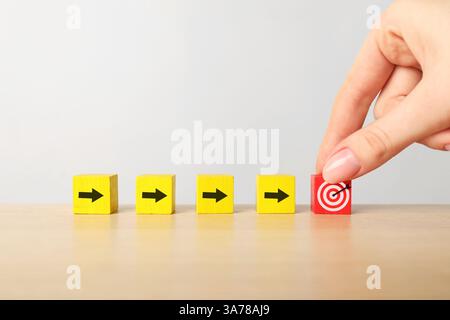 Ciblage. Femme mettant cube avec bullseye à d'autres avec des flèches sur la table en bois, gros plan Banque D'Images
