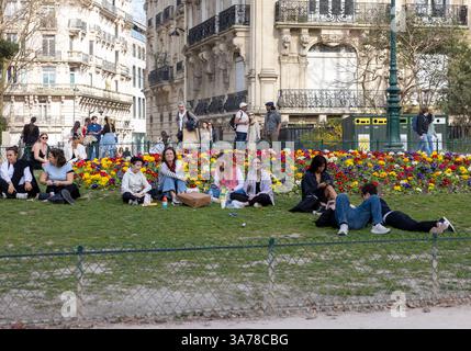 Paris, France - 20 mars 2025 : printemps à Paris. Les gens se détendent sur l'herbe à côté des plantes de Primula vulgaris qui fleurissent près du champs de mars Banque D'Images