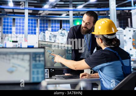 Ingénieur d'usine photovoltaïque pointant vers l'écran, montrant aux gestionnaires des moyens d'optimiser le flux de production. Employé de l'usine de panneaux solaires présentant le processus de fabrication du chef d'équipe sur l'écran d'ordinateur Banque D'Images