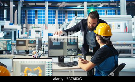 Directeur d'usine de fabrication de panneaux solaires montrant à l'ingénieur sur PC comment développer des prototypes pour de nouveaux systèmes d'énergie solaire. Chef d'équipe informant le technicien des nouveaux matériaux photovoltaïques, caméra A. Banque D'Images