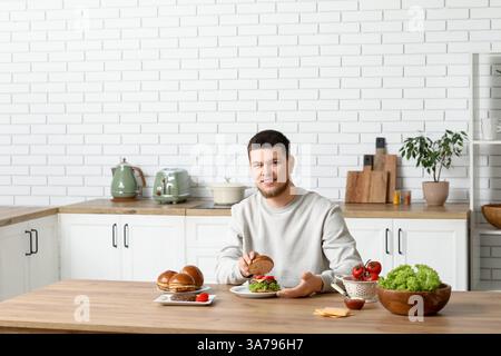Jeune homme faisant de savoureux hamburgers dans la cuisine Banque D'Images