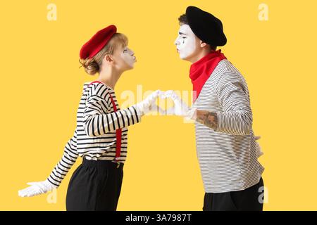 Couple de pantomimistes faisant le coeur avec leurs mains sur fond jaune Banque D'Images