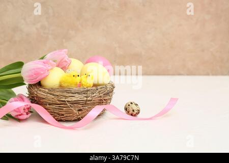 Nid avec des œufs de Pâques, des poussins et de belles fleurs de tulipes sur la table blanche Banque D'Images