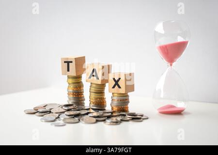 Mot de taxe sur les blocs de bois sur le dessus des pièces de monnaie, à côté de la minuterie de sable. Banque D'Images