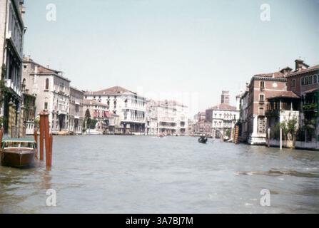 Une vue pittoresque sur le Grand canal de Venise, prise en 1965, avec ses palais historiques, ses gondoles et ses bateaux-taxis. Le canal, bordé d'une élégante architecture vénitienne, serpente au cœur de la ville, servant de voie navigable principale. Des gondoliers naviguent habilement sur le canal, tandis que des vaporettos (bateaux-bus publics) transportent les passagers à travers ce paysage intemporel. Banque D'Images