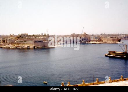 Cette photographie des années 1960 capture l’historique Fort Angelo et la ville fortifiée de Birgu (Vittoriosa), située dans le Grand Port de Malte. Bastion stratégique depuis des siècles, le Fort préparé Angelo se dresse fièrement à la pointe de la péninsule, avec le port environnant animé par l'activité maritime. Sur la droite, les navires amarrés et les grues reflètent le port de la Valette, illustrant l’importance de Malte en tant que plaque tournante maritime méditerranéenne. Banque D'Images