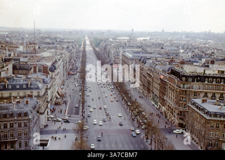 Une vue panoramique des années 1960 depuis le sommet de l'Arc de Triomphe à Paris, France, donnant sur l'avenue des champs-Élysées. Le grand boulevard s'étend au loin, flanqué d'élégants bâtiments de style haussmannien et animé par la circulation vintage et les piétons, capturant l'essence vibrante du Paris du milieu du siècle dernier. Banque D'Images