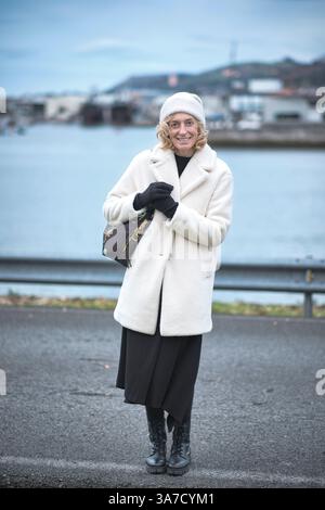 Touriste appréciant les vacances d'hiver à Colindres, Cantabrie, Espagne, portant un manteau blanc élégant, jupe noire et bottes Banque D'Images