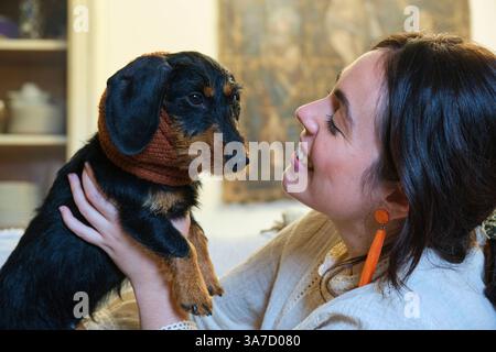 Heureuse jeune femme tenant son adorable teckel âgé à poil métallique portant des chauffe-oreilles, se regardant avec amour Banque D'Images