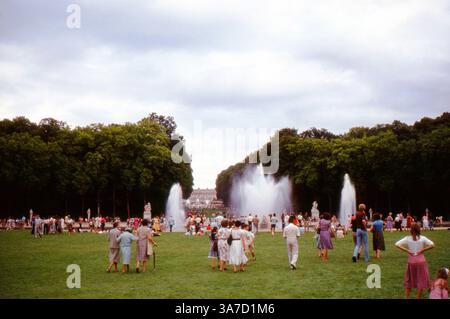 Les visiteurs se rassemblent autour des spectaculaires fontaines du bassin d’Apollon dans les jardins de Versailles, France. Ces scènes de fin d'été de 1984 montrent des foules appréciant la grandeur du jardin à la française, tandis que de puissants jets d'eau éclatent de la célèbre fontaine Apollon. Banque D'Images