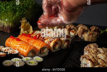 rouleaux de sushi de différents types que le cuisinier saupoudre de graines de sésame avant de servir Banque D'Images