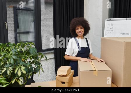 Une jeune femme sourit en emballant des boîtes dans son élégant appartement. Banque D'Images
