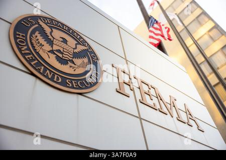 Signe FEMA (Federal Emergency Management Agency) et logo du département américain de la sécurité intérieure avec la lumière du soleil qui traverse les drapeaux américains derrière Banque D'Images