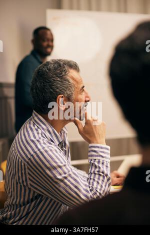 Vue latérale homme mature professionnel créatif assis la main sur le menton dans la salle de réunion au bureau Banque D'Images