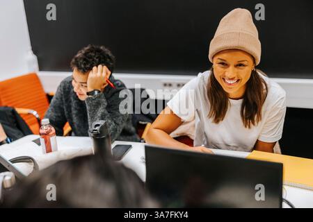 Vue en angle élevé de jeune femme heureuse portant un chapeau en tricot assis avec des amis dans la salle de classe à l'université Banque D'Images