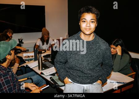 Portrait d'un jeune étudiant masculin debout avec la main dans la poche près de la table à la salle de classe du collège Banque D'Images