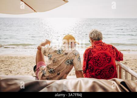Vue arrière d'un couple gay âgé assis à la plage le jour ensoleillé à Ko Lanta Banque D'Images