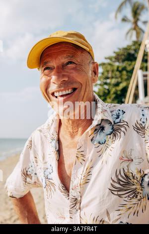 Homme âgé heureux portant un chapeau regardant loin à la plage Banque D'Images