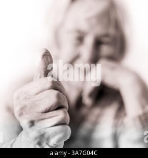 Contenu femme âgée de 96 ans donnant un pouce vers le haut et regardant la caméra. Concentrez-vous sur le pouce vers le haut, face floue. Vieillesse et concept de qualité de vie. Image en noir et blanc, teinte sépia. Banque D'Images