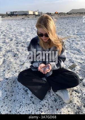 **'femme assise sur une plage de galets blancs unique, tenant de petites pierres dans ses mains. Banque D'Images