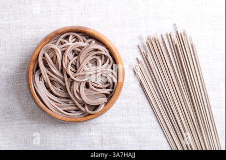 Nouilles soba réfrigérées et bouillies dans un bol en bois sur tissu de lin. Fines nouilles japonaises, fabriquées principalement à partir de farine de sarrasin. Banque D'Images