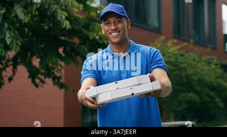Souriant homme café pizzeria travailleur livraison homme Africain américain Guy courier tenant carton boîte colis pizza fast food livrer repas regardant Banque D'Images