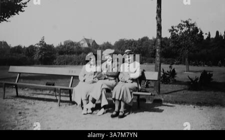 1936, un groupe de deux dames et un gentleman en manteaux et chapeaux, assis sur un banc à Bad Godesberg, un quartier de Bonn, en Allemagne, situé le long du Rhin dans l'état de Rhénanie du Nord-Westphalie. Il est connu pour sa beauté pittoresque et son importance culturelle. D'une collection de photographies amateurs non attribuées dans la plage de dates, 1929-1936, qui comprennent les vacances britanniques et européennes. La plupart des images originales étaient d'environ 3 ½ x 2 pouces. Banque D'Images