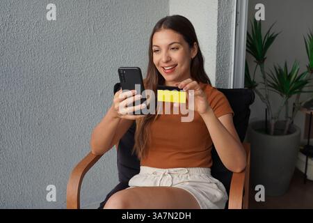 Souriante jolie femme regardant le téléphone montrant la carte de crédit à la caméra Banque D'Images