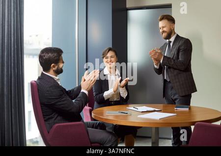 Équipe de gens d'affaires heureux assis ensemble autour de la table de bureau, faisant des applaudissements Banque D'Images