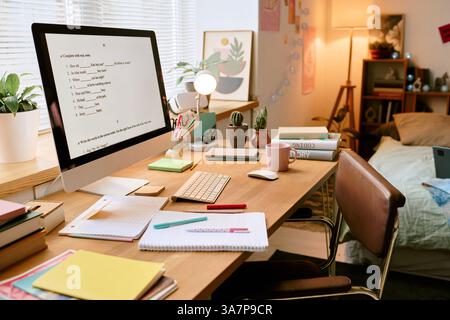 Espace de travail avec ordinateur moderne, notes et livres, situé dans un bureau à domicile confortable. Lit et objets décoratifs en arrière-plan. Configuration propre et accueillante Banque D'Images