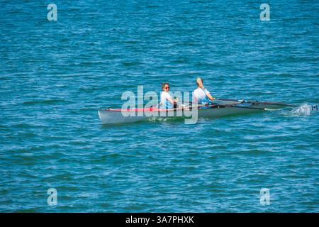 Deux individus propulsent leur bateau à rames à double écluse à travers la surface ondulée de l'eau Banque D'Images