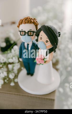 Un charmant gâteau de mariage comprend une mariée et un marié masqués, mettant en valeur une célébration moderne avec des fleurs. Banque D'Images