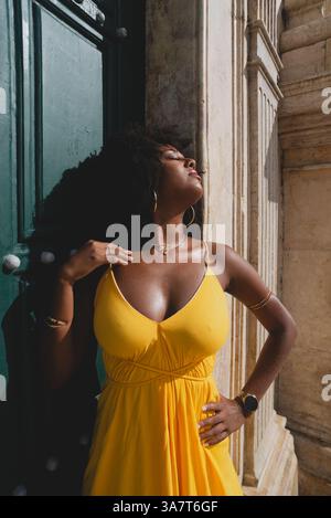 Belle femme noire avec des cheveux de corbeau portant une robe jaune posant pour la photo contre la grande porte verte de l'église. Heureux et souriant Banque D'Images
