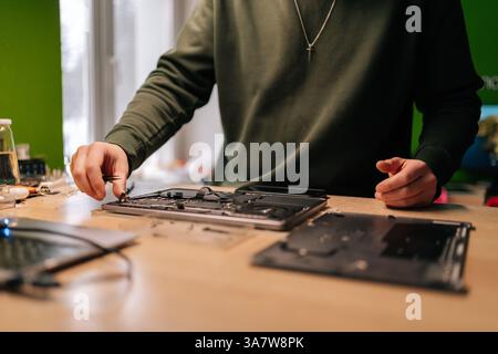 Cliché recadré d'un ingénieur électronique utilisant des pinces à épiler, fixant des composants sur la carte mère de l'ordinateur portable, effectuant des opérations de maintenance et de dépannage en réparation Banque D'Images