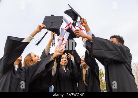Groupe de diplômés multiethniques joyeux célébrant leur graduation en jetant leurs mortarboards et diplômes dans l'air Banque D'Images