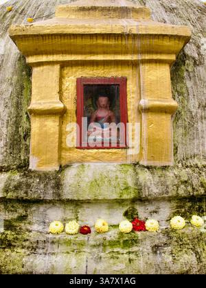 Petite statue de Bouddha dans une niche sur le dôme strié de mousse du Boudhanath Stupa, encadrée par des offrandes de souci et de chrysanthème. Banque D'Images