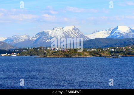 Vue sur la côte du Hardangerfjord avec des maisons norvégiennes traditionnelles colorées et des montagnes enneigées en arrière-plan. Banque D'Images