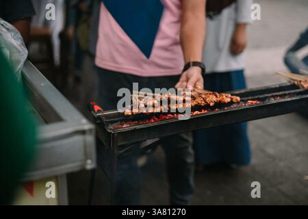Gros plan d'une grillade satay sur charbon de bois chaud sur un stand de nourriture de rue. Ces brochettes de poulet savoureux sont une délicatesse populaire d'Asie du Sud-est. Rue Banque D'Images