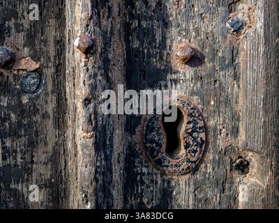 Gros plan d'un trou de serrure sur une vieille porte en bois avec de la peinture noire usée et des rivets altérés. Banque D'Images