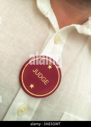 Gros plan d’un homme portant une chemise en lin blanc avec un badge « juge » épinglé sur la poitrine, visage non visible Banque D'Images