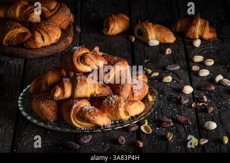 Un ensemble de petits pains doux, brun doré fourrés de chocolat riche et de pistache crémeuse, servis élégamment sur des assiettes en verre. Banque D'Images