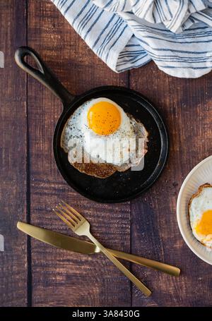 Vue de dessus oeuf frit dans la casserole avec couverts assiette sur la table en bois. Banque D'Images